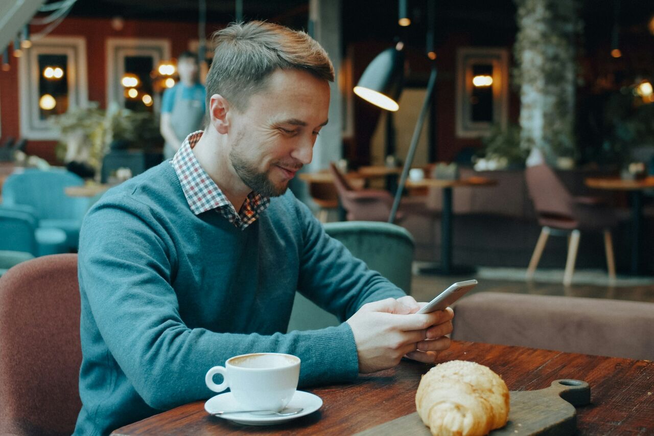 A man at a cafe table reading something on his smartphone
