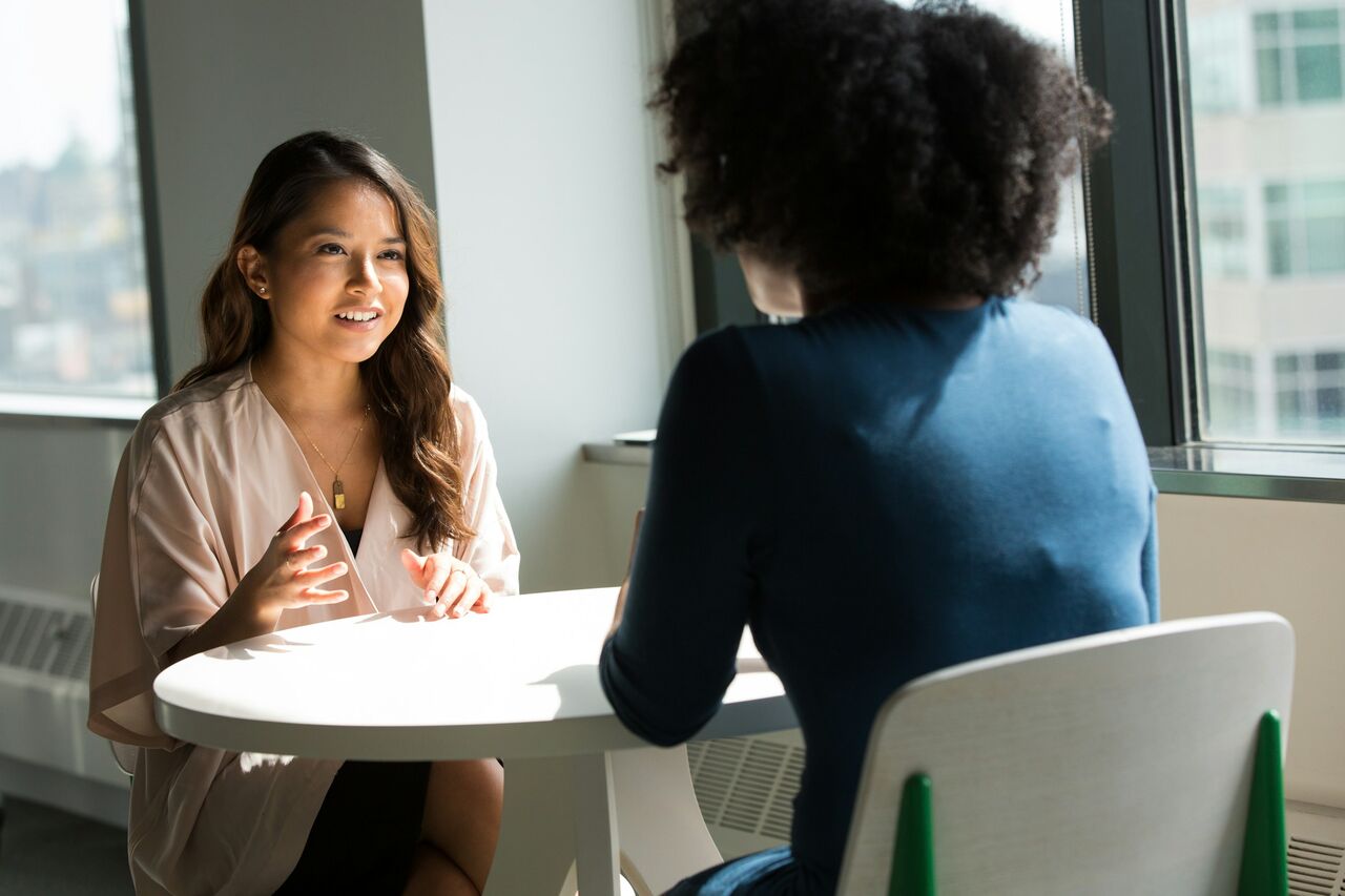 A health coach talking with a client across a small table by a bright window